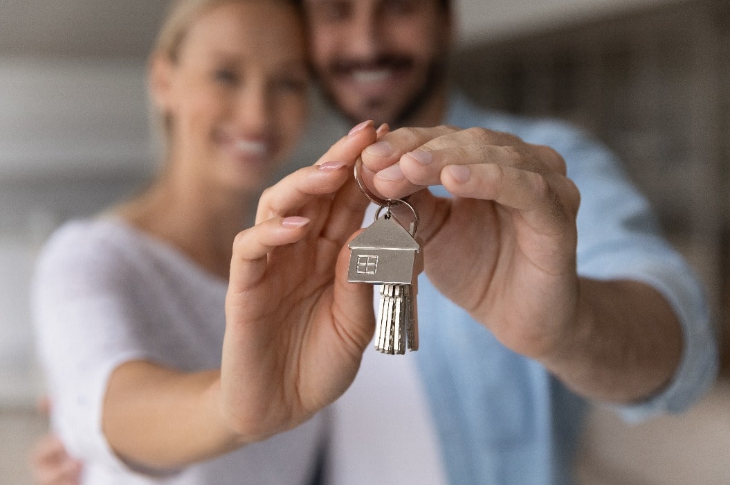 Close up crop of happy Caucasian couple show keys buy or rent first shared home together. Man and woman spouses renters celebrate moving relocating to new house. Relocation, real estate concept.