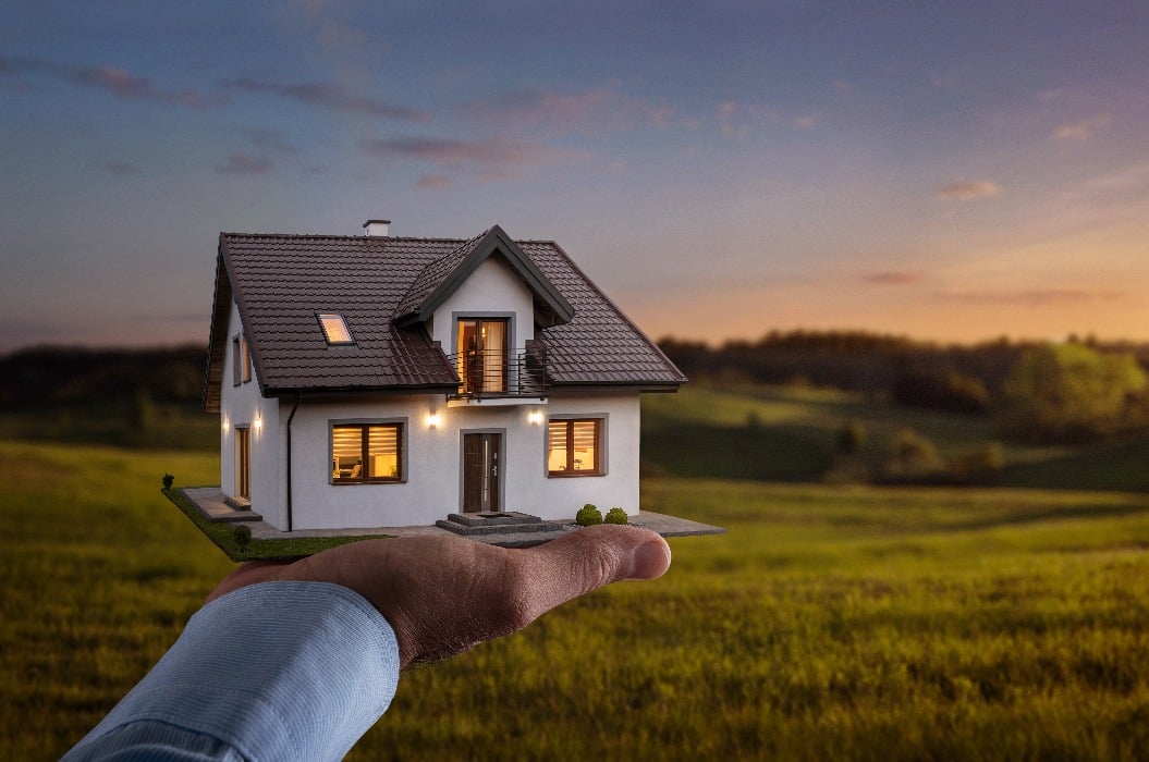 Concept of buying or building new home. Male hand showing, offering a new dream house at the empty field with copy space