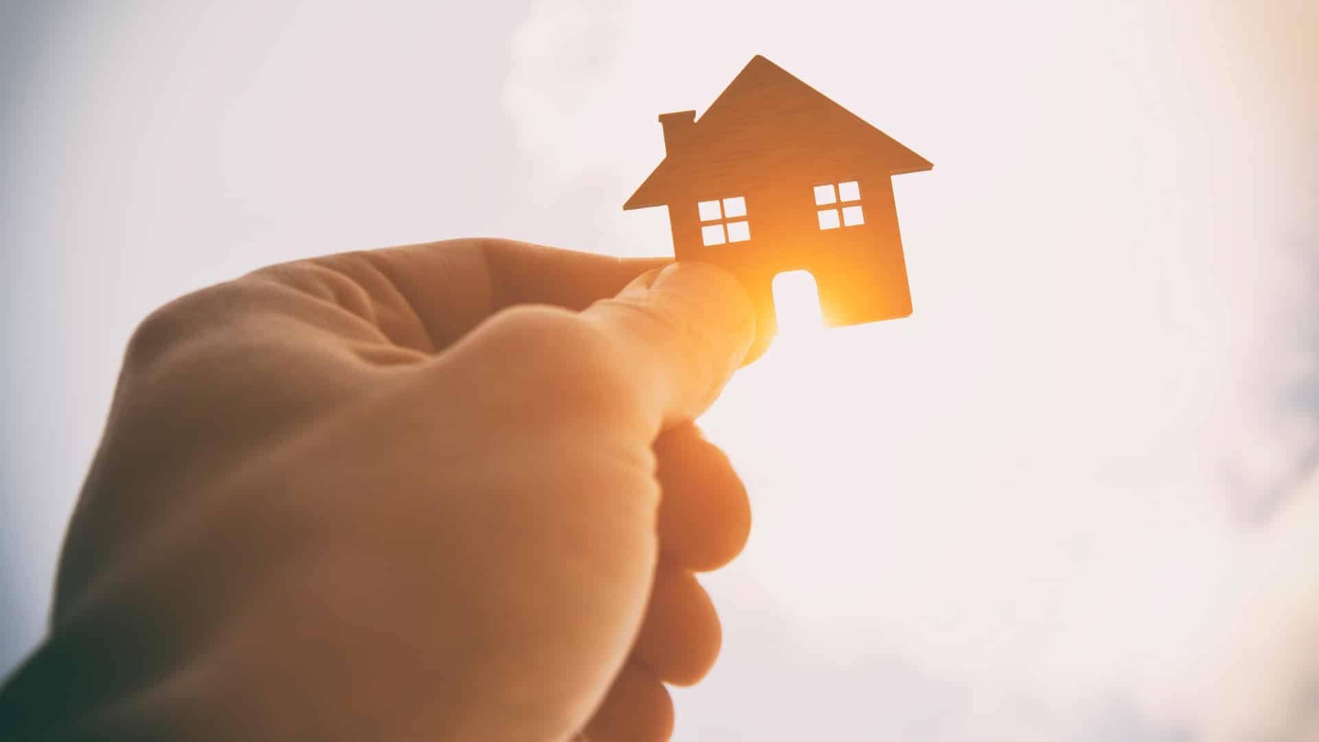 Man's hand holds wooden flat house against the sun