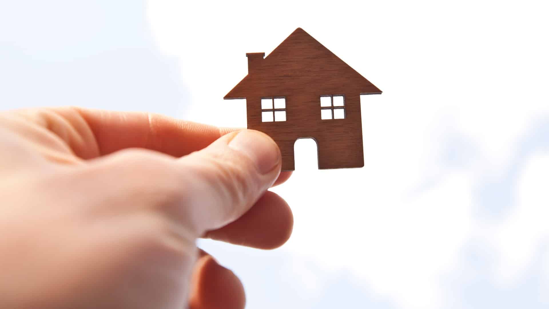 Man's hand holds wooden flat house against the sun