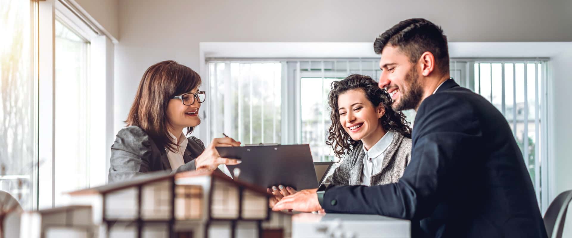 Side view of young happy family sitting in consulting office, making property purchase. Female realtor helping business couple do financial investment. Installment payment, mortgage, loan concept